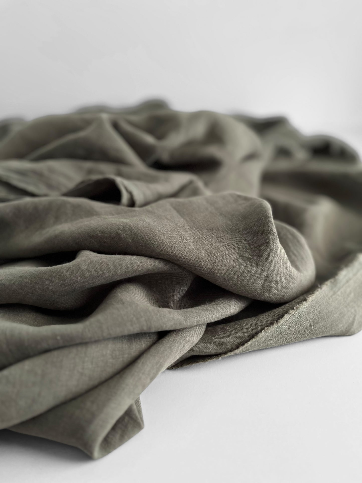 Folded dusty green linen fabric on a white background